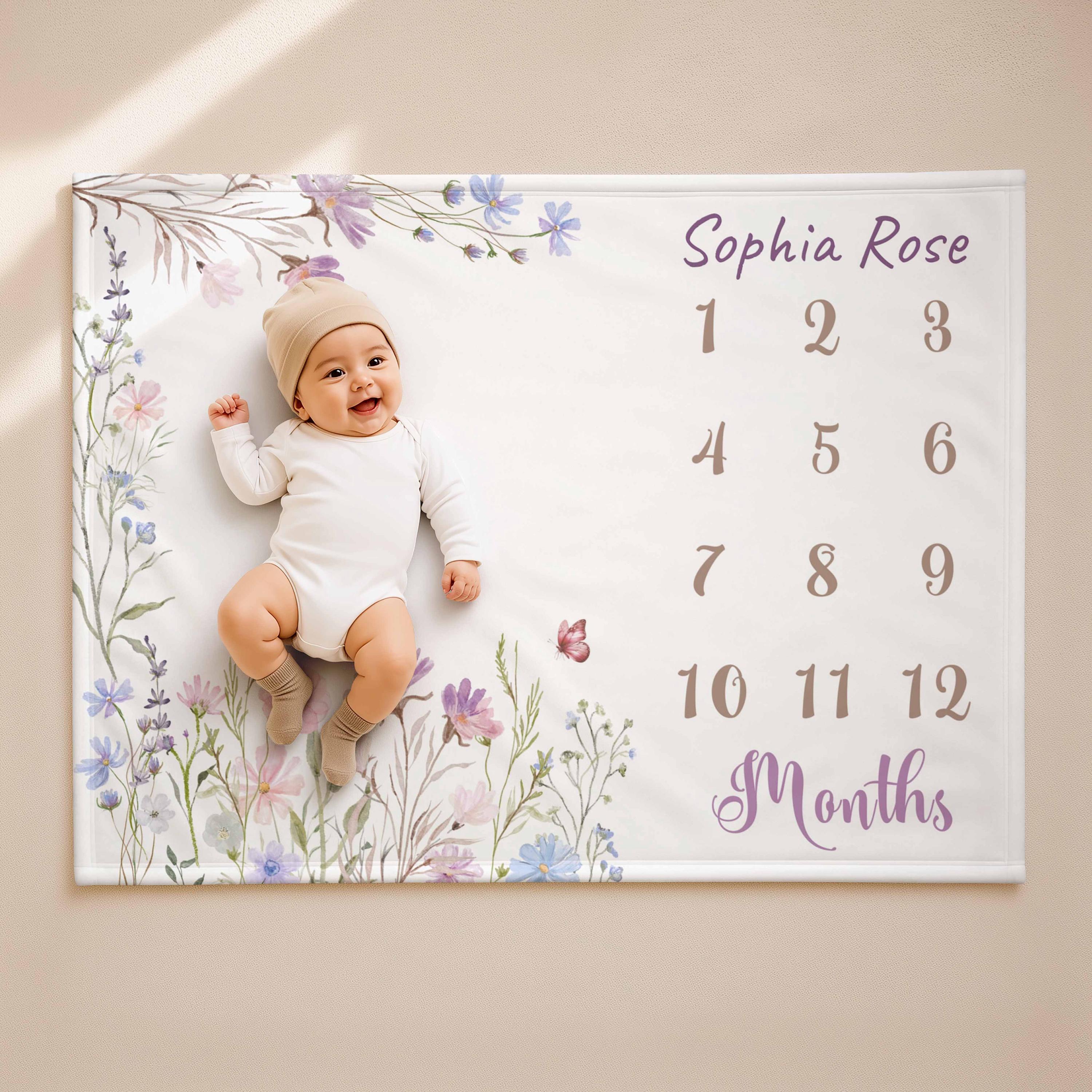 A baby lying in the centre of a wildflower milestone blanket printed with her name