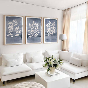 Three navy prints of white leaves above a white sofa