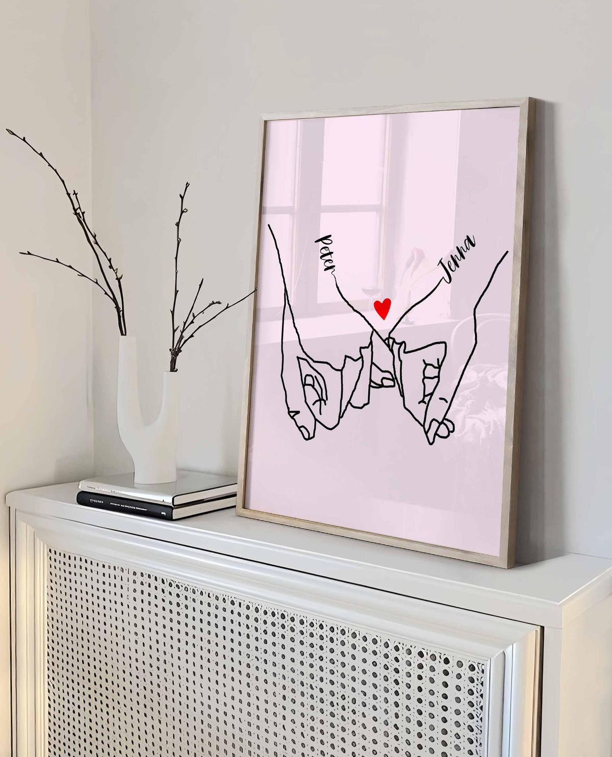 Pink pinky promise couple print in a tall oak frame on a white radiator cabinet with a branch vase