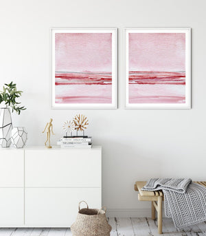 Two blush and rose watercolour seascapes above a white sideboard