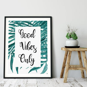 Good Vibes Only framed by teal palm leaves in a black frame beside a stool