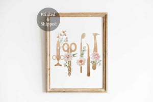 Rose gold dental tools standing upright with blush flowers, in a wooden frame